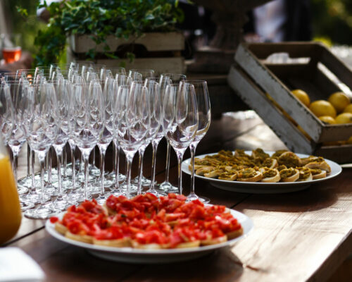 White dishes with sandwiches stand on wooden table before empty champagne flutes